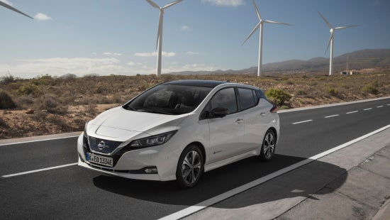 Nissan vehicle driving on road, wind turbines in the background | Jim Click Nissan in Tucson AZ